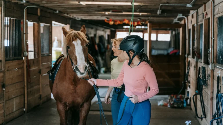 Principiante con casco aprendiendo a manejar un caballo junto a su monitora
