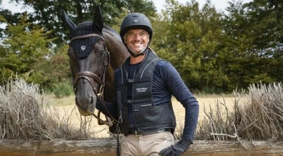 Jinete con chaleco protector junto a su caballo